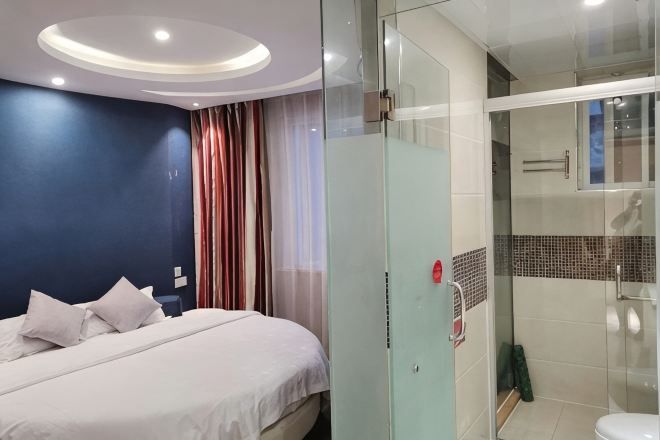 Quarto de hotel com cama, box de chuveiro de vidro e design de banheiro moderno.