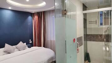 Quarto de hotel com cama, box de chuveiro de vidro e design de banheiro moderno.