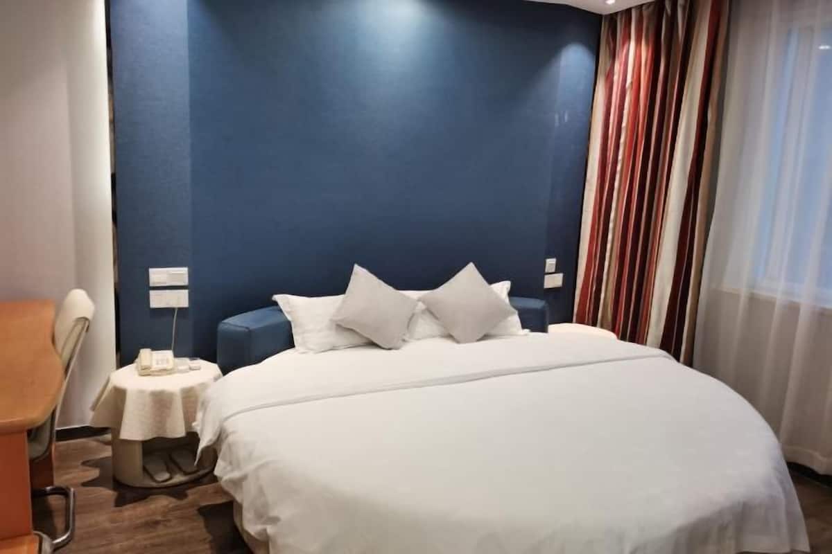 A hotel room with a large bed, a small bedside table with a phone, and a chair.