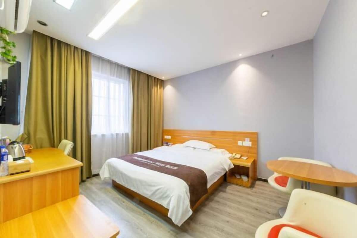 A hotel room with a bed, a desk, a chair, a small table, and a nightstand.