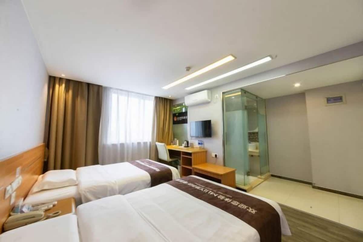 A hotel room with two beds, a desk, a chair, a television, and a glass partition.