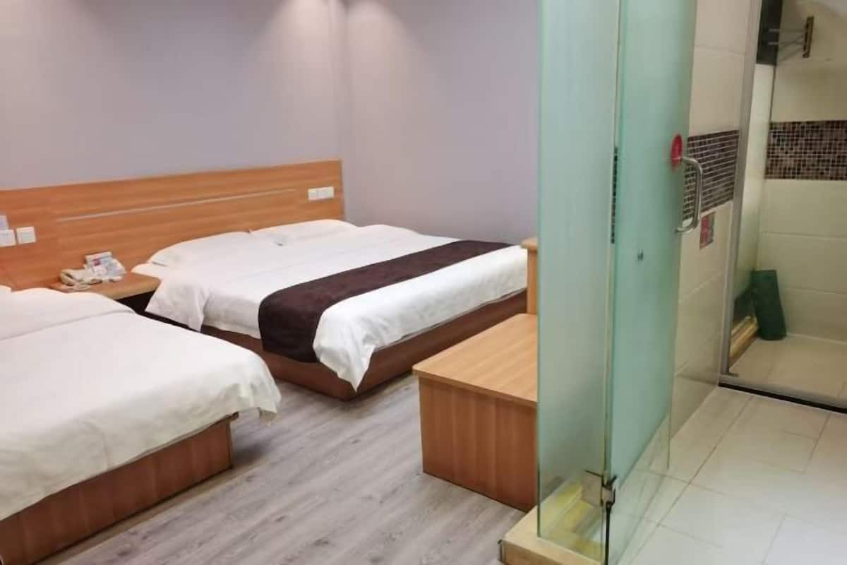 A hotel room with two beds, a wooden headboard, a small wooden table, and a glass shower enclosure.