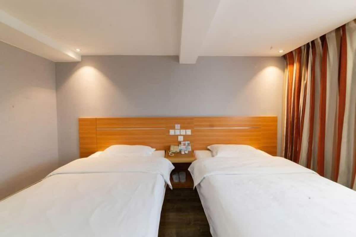 A hotel room with two single beds, a wooden headboard, a nightstand with a telephone, and a curtain on the right side.