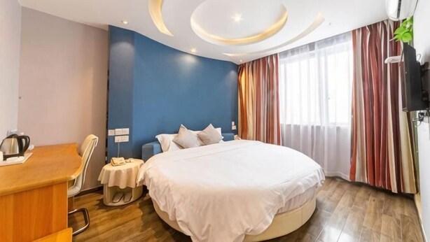 Habitación de hotel con cama, escritorio, silla, mesita y ventana con cortinas.