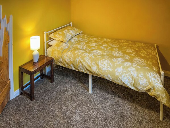 A single bed with a floral bedspread in a room with yellow walls and a wooden floor.
