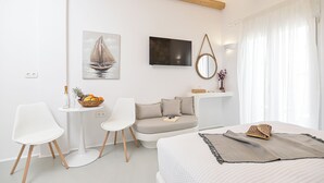 Un dormitorio moderno con una cama, un sofá, una mesita con una cesta de fruta y un televisor.