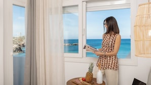 Una persona leyendo un periódico junto a una ventana con vista al mar.