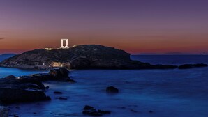 Escena costera con un edificio blanco destacado sobre un promontorio rocoso, con vistas a aguas tranquilas.