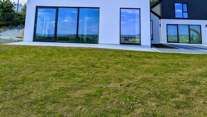 A modern two-story house with large windows and a flat roof, set against a clear blue sky.