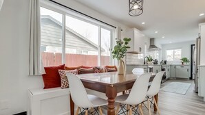 A modern kitchen with white cabinets, a dining area with a wooden table and white chairs, and a view of the outside through large windows. - The Western Retreat | Hot Tub & Spacious Yard (Westminster)