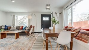A modern living room with a sofa, dining table, chairs, a coffee table, and a rug. - The Western Retreat | Hot Tub & Spacious Yard (Westminster)