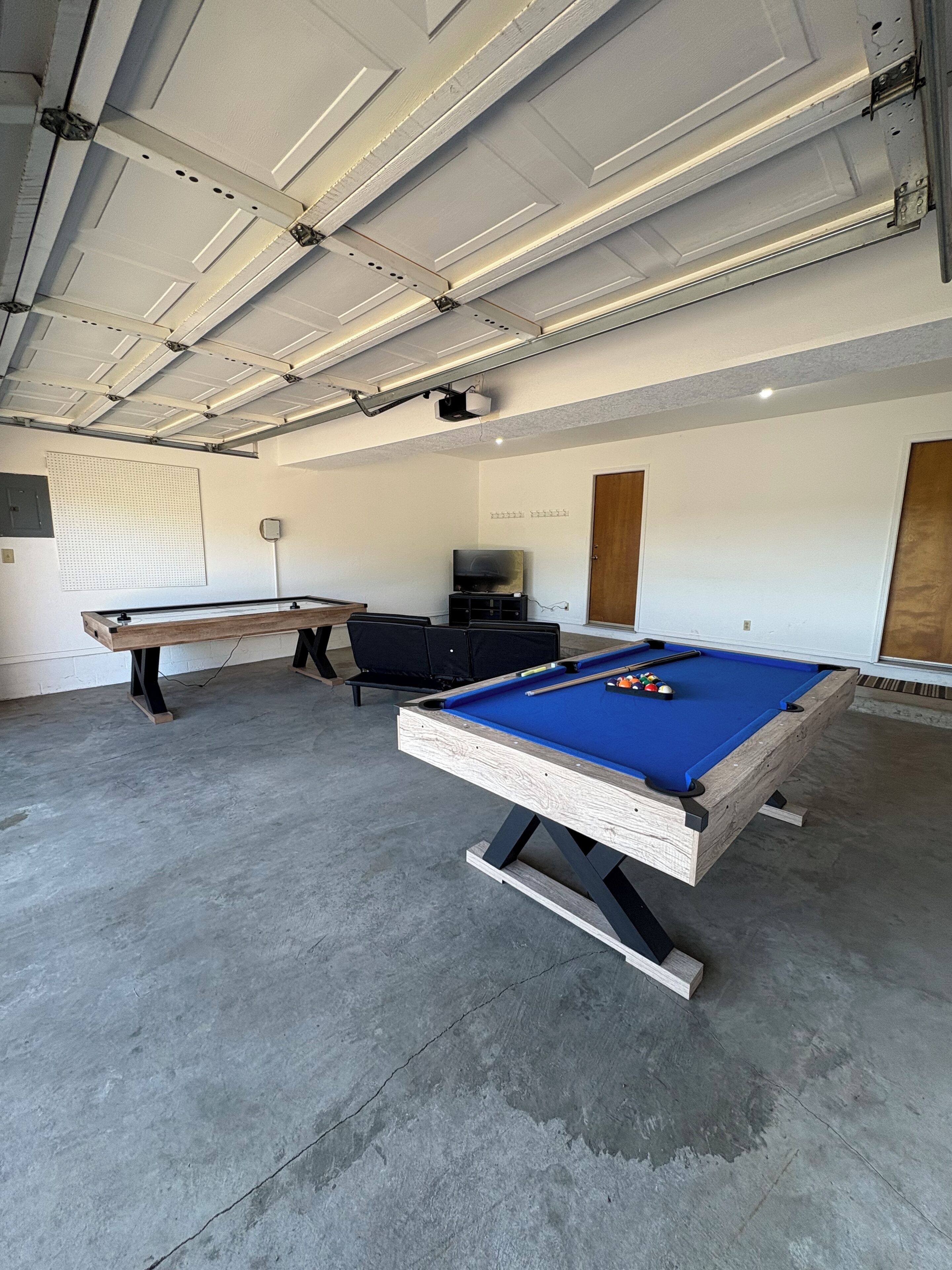 A pool table in a room with a concrete floor, a ceiling with exposed beams, and a wall-mounted TV.