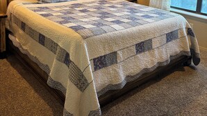 A bedroom with a large bed, a ceiling fan, a nightstand with a lamp, a window with curtains, and a wall-mounted artwork. - Bring the whole family to enjoy hot tub, deck & beautiful mountains in Ruidoso (Ruidoso)