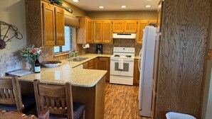 A kitchen with wooden cabinets, a granite countertop, a stove, a refrigerator, and a dining area with chairs. - Bring the whole family to enjoy hot tub, deck & beautiful mountains in Ruidoso (Ruidoso)