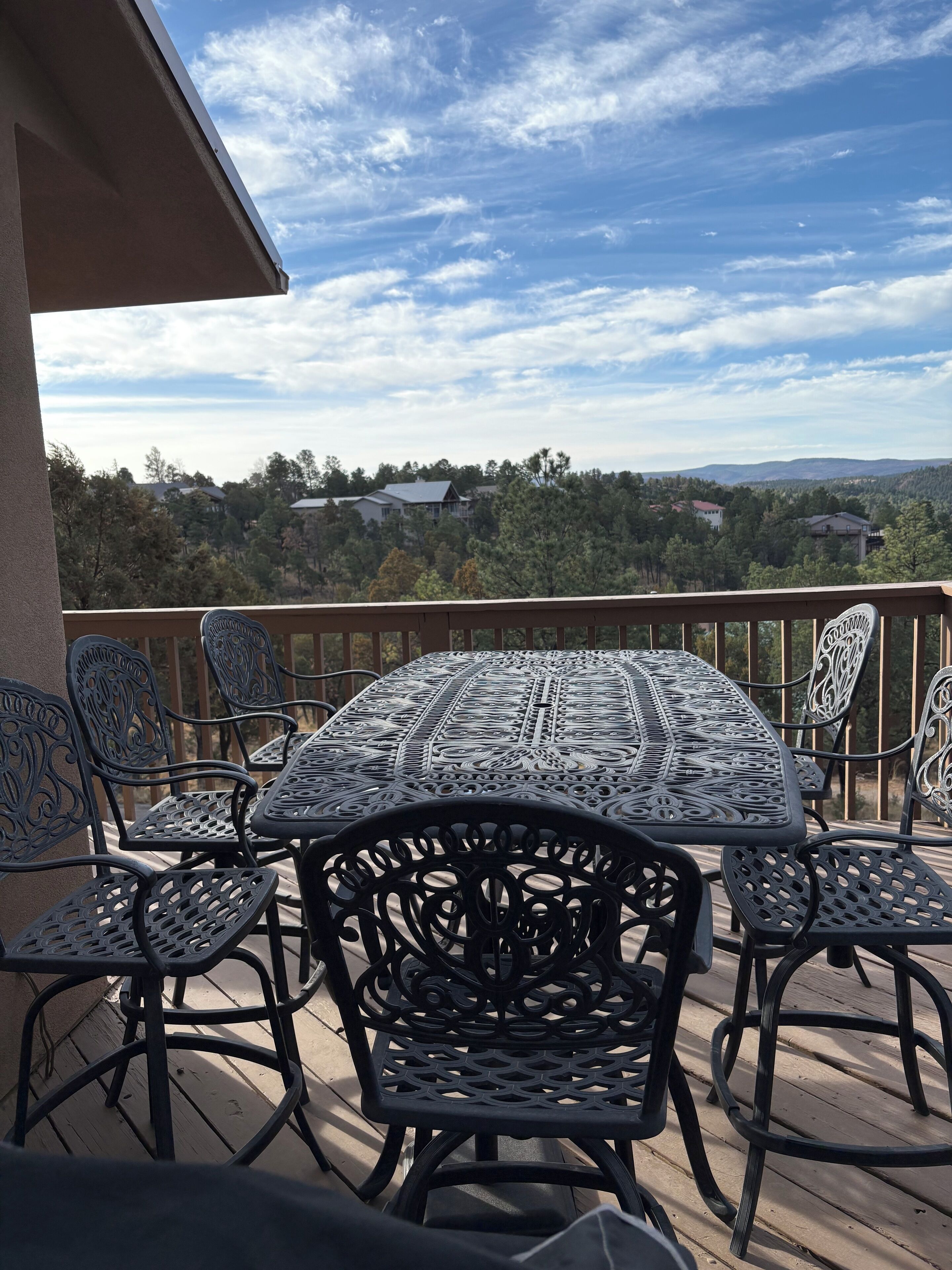 A deck with a table and chairs, overlooking a scenic landscape with trees and houses.