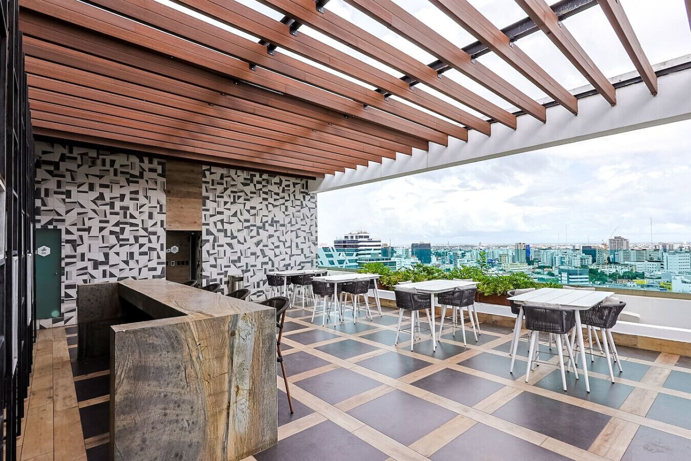 En tagterrasse med et træpergola, et mønstret væg og udsigt over byen.