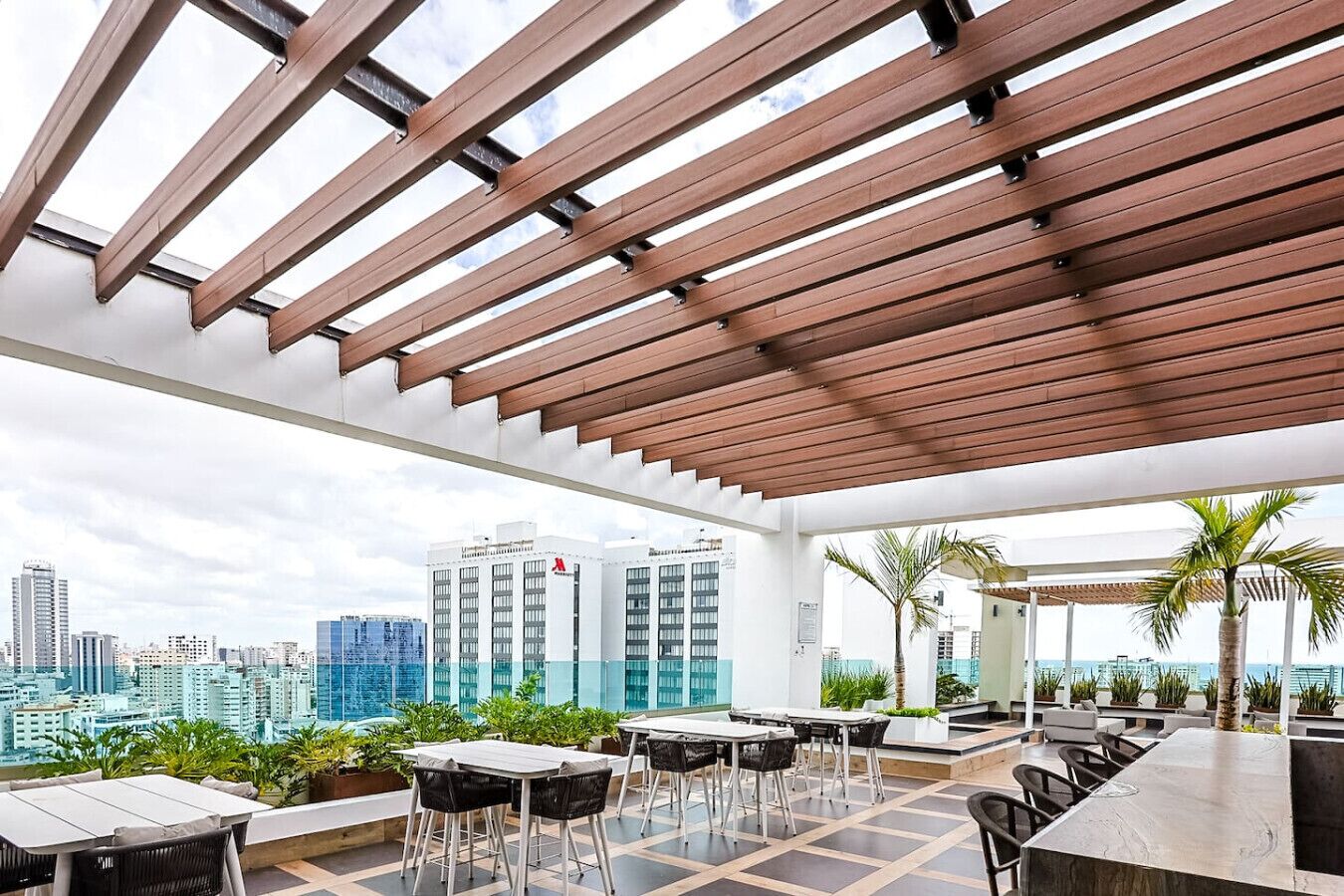 Terraza al aire libre con mesas y sillas, con vistas a un paisaje urbano con edificios altos.