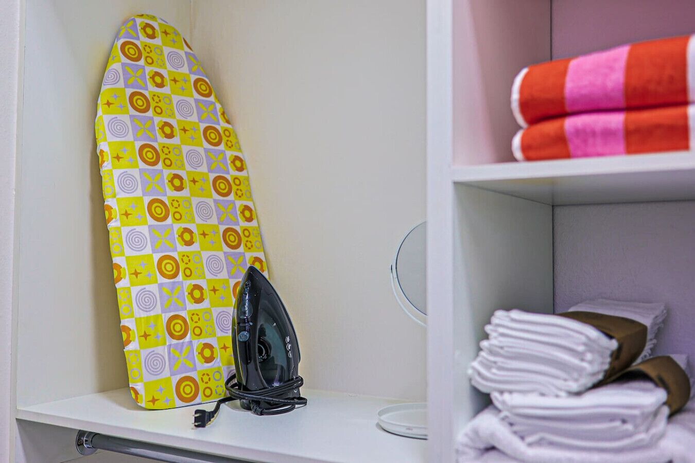 Un área de almacenamiento ordenada con una tabla de planchar, un planchador y toallas dobladas con cuidado.
