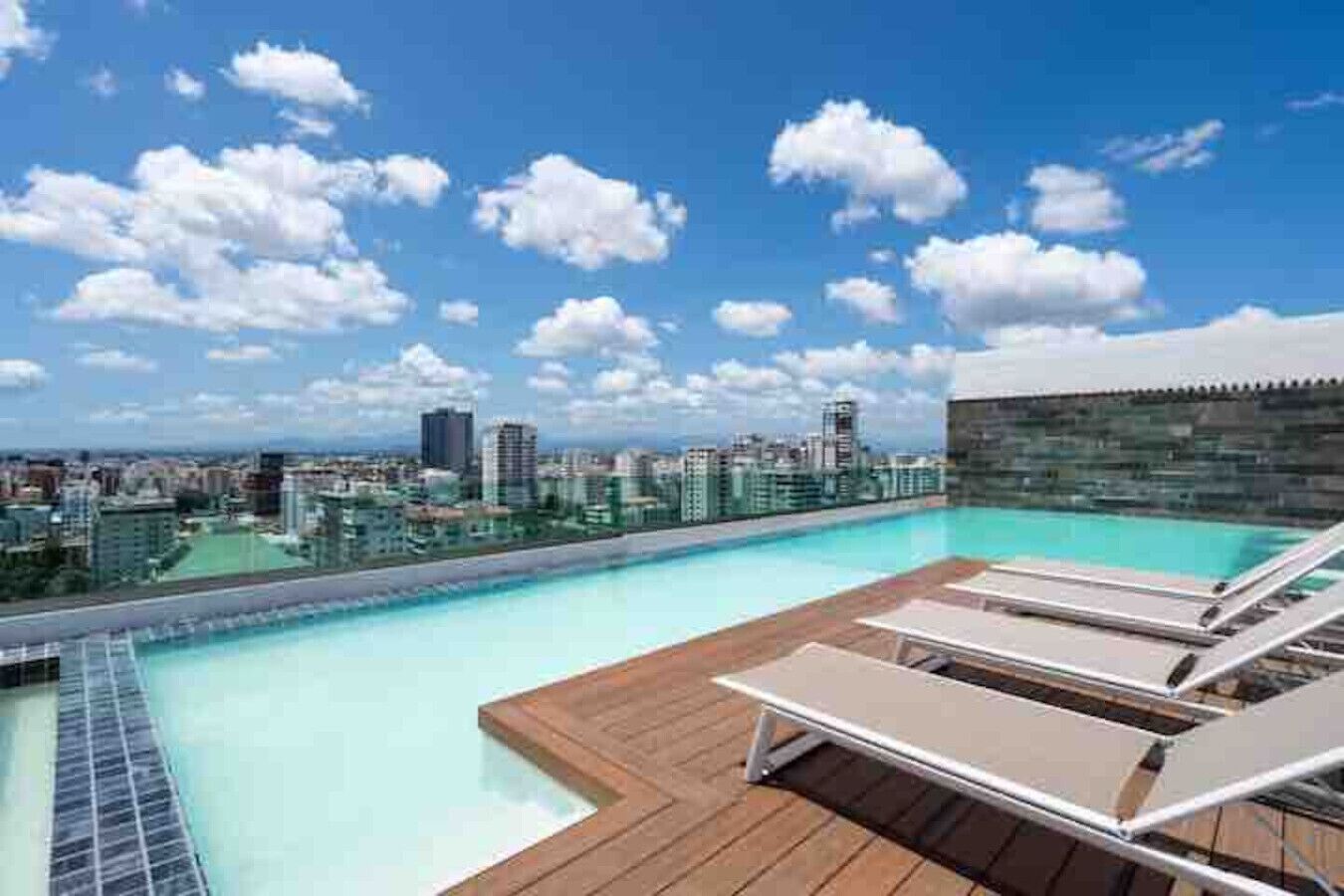 Una piscina en la azotea con sillones de descanso y vista a la ciudad.