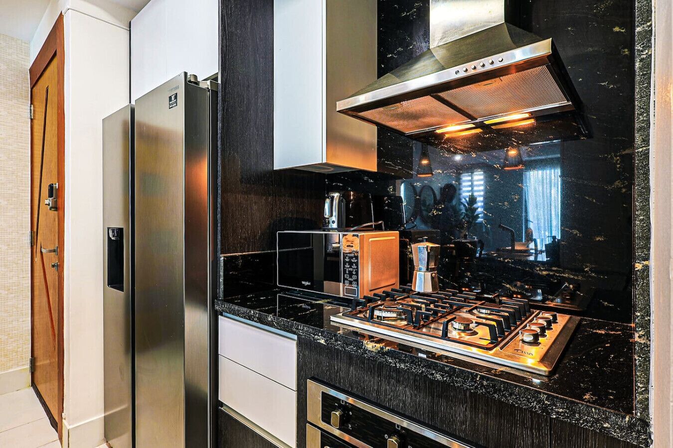 Una cocina moderna con un refrigerador de acero inoxidable, una estufa a gas y una cafetera.