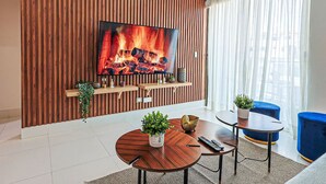 Un salon moderne avec un téléviseur à écran plat fixé à un mur en bois, une table basse ronde en bois, deux fauteuils bleus et une petite table d’appoint avec une plante.