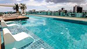 Une piscine à débordement située sur le toit, avec une eau d’un bleu cristallin, des chaises longues et une vue panoramique sur la ville.