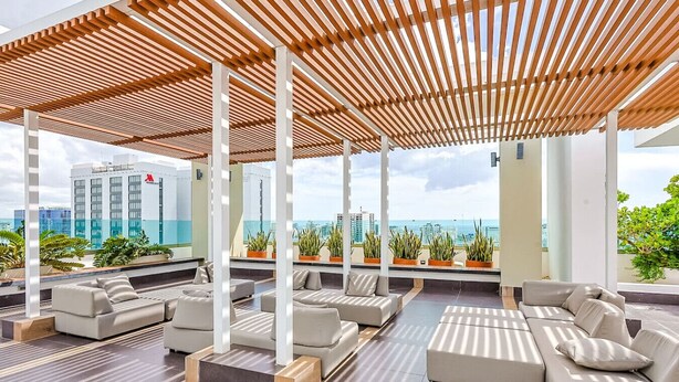Un salon sur le toit doté de plusieurs espaces de détente, d’une pergola en bois et offrant une vue sur le panorama urbain.