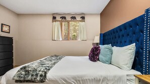 A bedroom with a bed, a blue headboard, a window with curtains, and a wall-mounted lamp. - Golden Summit | Air Hockey | Wood Fireplace | Pets (Radium Hot Springs)