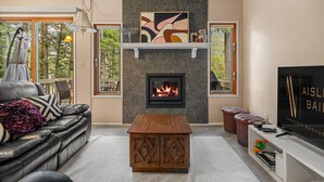 A modern living room with a fireplace, leather sofa, wooden coffee table, and a TV on a stand. - Golden Summit | Air Hockey | Wood Fireplace | Pets (Radium Hot Springs)