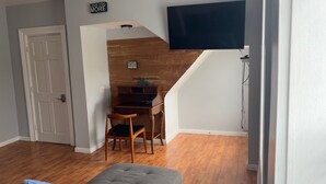 Una habitación con un escritorio de madera, una silla, un televisor montado en la pared y una escalera que sube a otro nivel.