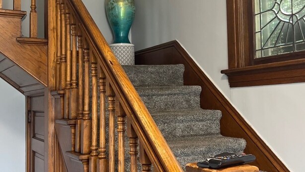 Una escalera de madera con un jarrón de ramas y un control remoto en la barandilla.