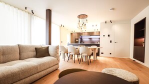 A modern living room with a sofa, dining table, and chairs. There is a kitchen area in the background with cabinets and a microwave. - Apartment Near Durbuy Old Town & Golf (Durbuy)