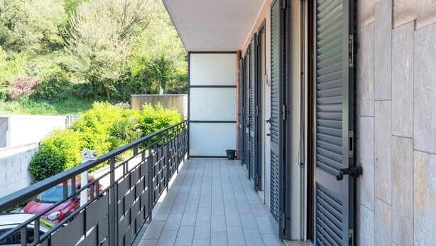 A balcony with a tiled floor, a metal railing, and a view of greenery and parked cars. - Ideal for exploring the Amalfi Coast, Capri, Sorrento, Pompeii, Paestum and more (Salerno)