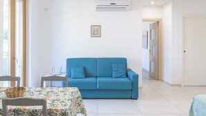 A living room with a blue sofa, a small table with a floral tablecloth, and an air conditioning unit on the wall. - Ideal for exploring the Amalfi Coast, Capri, Sorrento, Pompeii, Paestum and more (Salerno)