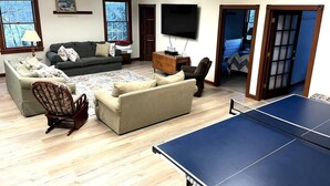 A living room with a ping pong table, sofas, a chair, a television, and a door leading to another room.
