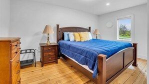 Una camera da letto con un letto in legno, due comodini con lampade, una cassettiera e una finestra vista verde.