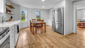Una cucina moderna con pavimento in legno, mobili bianchi, un frigorifero in acciaio inossidabile e un tavolo da pranzo con sedie.