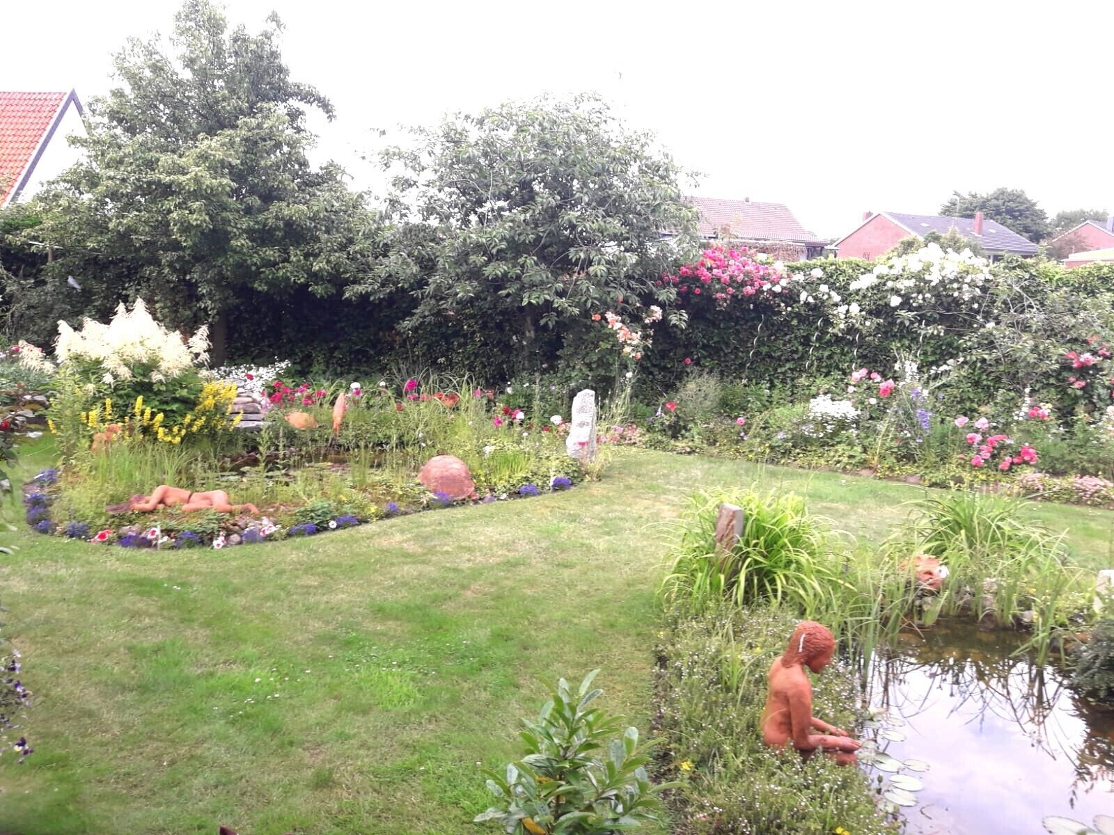 A garden with a pond, statues, and various plants.
