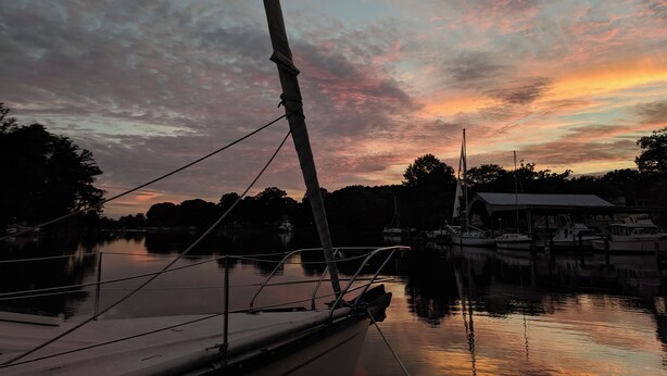 A calm harbor at sunset with a sailboat docked, reflecting the sky's colors. - Creekside Oasis (Lusby)