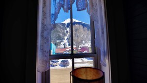Ein Fenster mit Blick auf einen schneebedeckten Berg und geparkte Autos vor dem Haus.