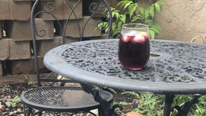 A round metal table with a decorative pattern, a glass pitcher with a dark liquid, and a smaller round table beside it.