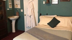 A bedroom with a bed, a bedside table, a lamp, a sink, and a robe hanging on a door. - Villa Dallavalle Inn Room 5 (Silverton)