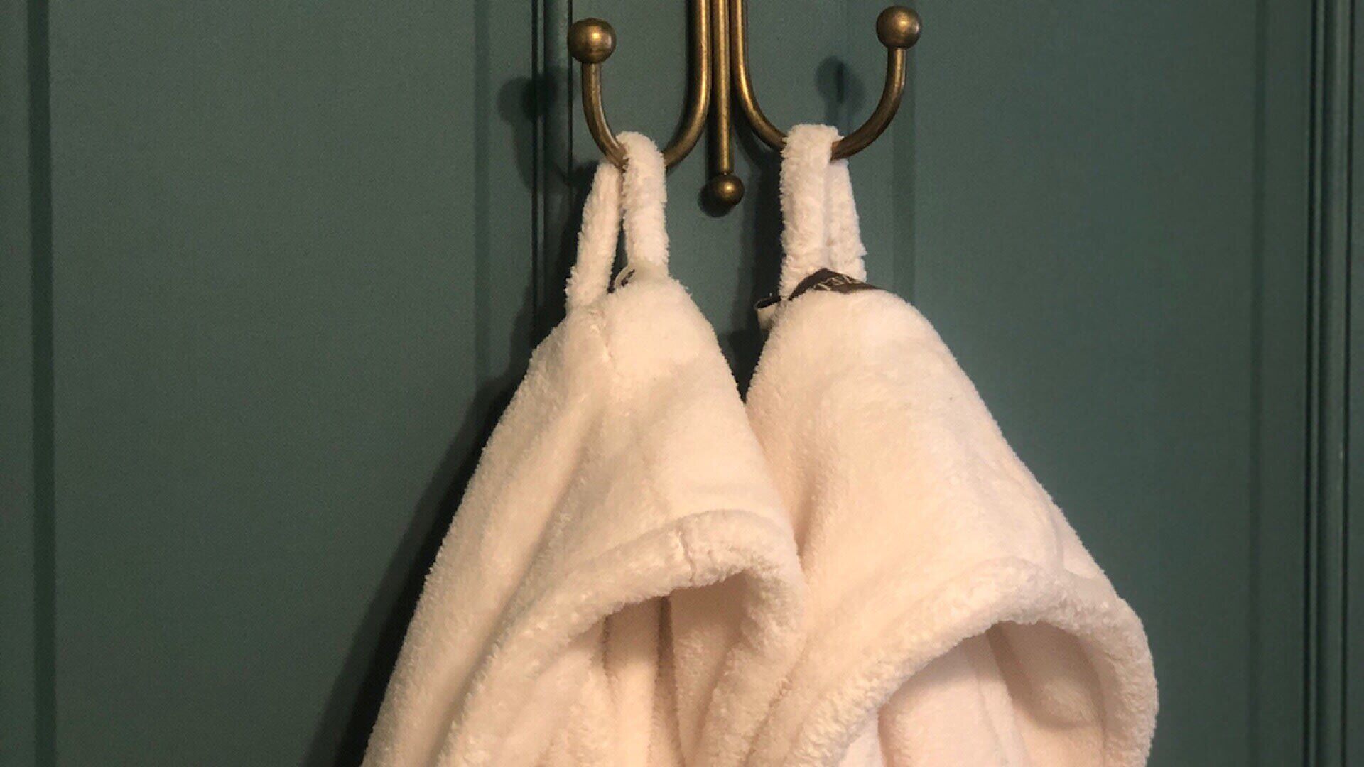 A towel rack with two white towels hanging on a teal-colored door.