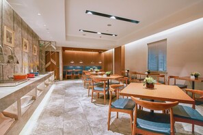 Un restaurante con varias mesas y sillas de madera, suelo de mármol e iluminación colgante.