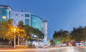 Un edificio moderno con fachada de vidrio curva, rodeado de árboles y farolas.