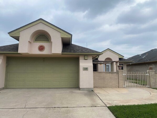 A residential house with a green garage door, a small porch, and a brick wall.