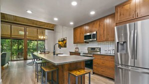 Une cuisine moderne avec des meubles en bois, des appareils en acier inoxydable et un grand îlot central doté de tabourets.