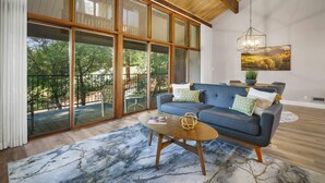 Un salon moderne doté d’une grande porte vitrée donnant sur un espace extérieur, d’un canapé bleu et d’une table basse en bois.