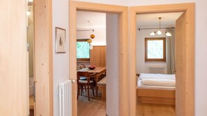 Une pièce de taille modeste, avec un plancher en bois, un lit, une table et des chaises, et une fenêtre.