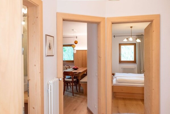 A compact room with a wooden floor, a bed, a table with chairs, and a window.